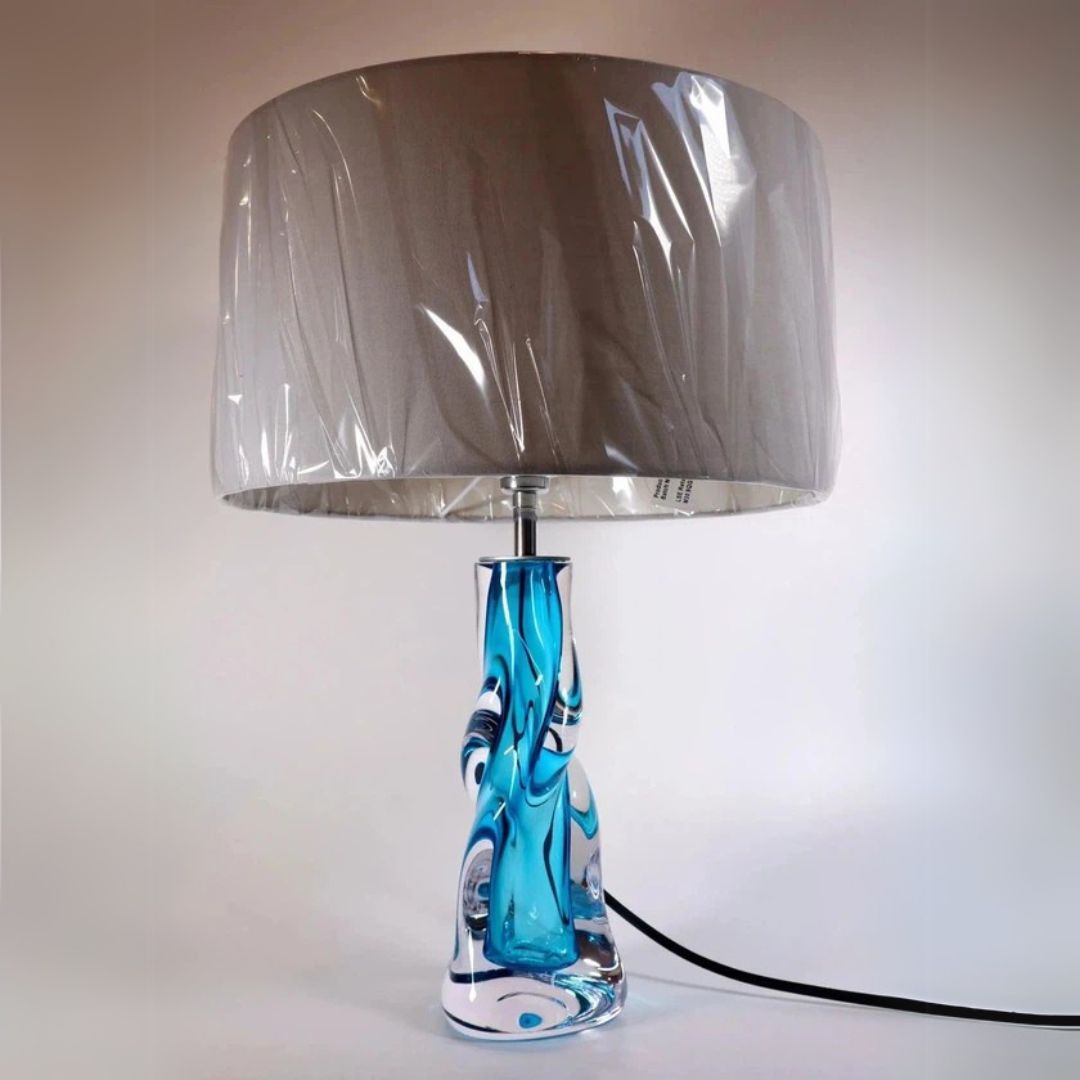 A hand-blown glass Vortex table lamp with a blue and clear design at the base, topped with a grey lampshade.